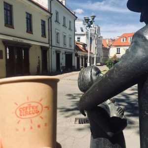 Coffee Circus Vilnius takeaway cup held on historic Vilnius street, showing specialty coffee on the go in European old town setting