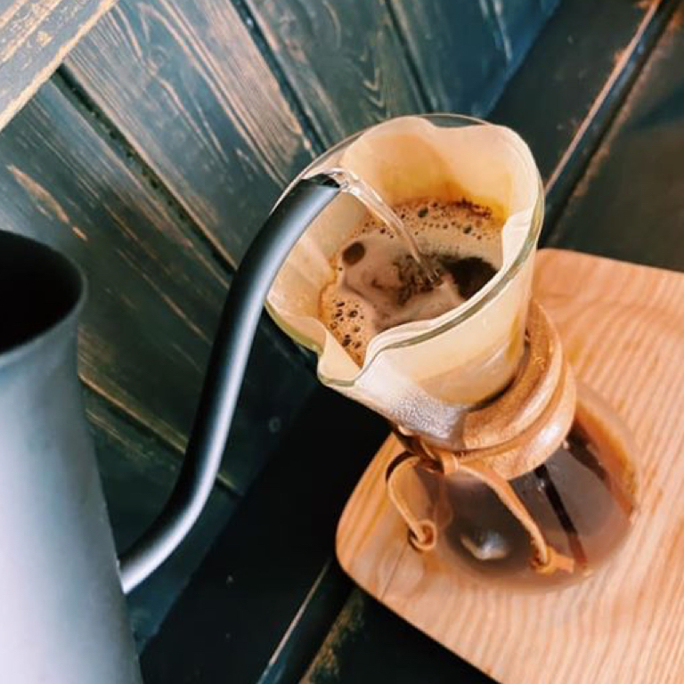 Chemex pour-over coffee brewing with filter and fresh grounds on wooden surface, showcasing Coffee Circus specialty coffee preparation method