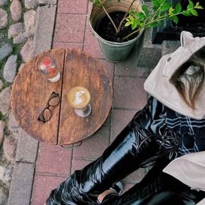 Coffee Circus cappuccino with latte art on rustic wooden table, outdoor cafÃ© setting with cobblestone patio and customer relaxing with specialty coffee