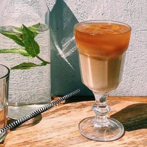 Coffee Circus layered iced coffee drink in elegant stemmed glass on wooden table, showcasing specialty cold coffee with distinct milk and espresso layers