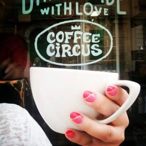 Person holding white coffee cup at Coffee Circus specialty coffee shop